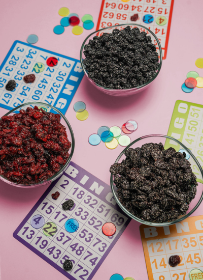 Fruiter all-natural dried blueberry, cherry, and cranberry candy in bowls surrounded by colorful game boards. Fruiter candy comes in sweet, sweet and sour, and super sour varieties.