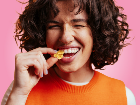 A young woman smiling and wrinkling her nose while tasting a Fruiter Sweet and Sour all-natural fruit snack. Fruiter dried blueberry, cherry, and cranberry candy comes in sweet, sweet and sour, and super sour varieties.